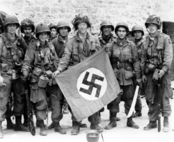 American paratroopers, among the first to make successful landings on the continent, holds a Nazi flag captured in a village assault. Utah Beach, St. Marcouf, France. 8 June 1944