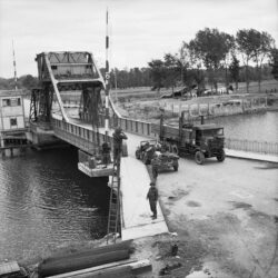 Pegasus Bridge, 9 June 1944. Vehicles including a Royal Signals jeep & trailer and a RASC Leyland lorry on 'Pegasus Bridge' over the Caen Canal at Benouville. The signallers are fixing telephone lines across the bridge.
Photograph: Sergeant Christie. No. 5 Army Film and Photo Section, Army Film and Photographic Unit
Imperial War Museum Catalogue Number: B 5288