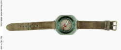 Wrist compass : Trooper D R Barnby, 2 Squadron, Special Air Service Regiment.
Description: Wrist mounted magnetic compass, finished in medium green aluminium and fitted with a worn olive green nylon wrist strap. The compass has degrees etched into the edge of the rotating dial and mils indicators every 10 mils etched into the body. A small arrow is etched into the top of the compass body, next to the wrist strap. An index pointer consisting of a pair of 2 mm high vertical lines, separated by a small 1 mm diameter dot are stamped into the rotating dial. An orienting arrow and parallel orienting lines, marked in red, are fitted to the base of the compass on a rotating housing.
The wrist strap has seven 2 mm diameter metal bounded holes centrally placed for adjusting the size. An indent with remnants of an unknown blue-green substance (possibly verdigris) is on the fourth hole. This indent corresponds with the wrist band metal buckle. The wrist band is fitted with a pair of horizontally arranged 5 mm diameter bands for securing the excess wrist band length. One of these horizontal bands is adjustable along the wrist band and the other, in a lesser condition, is stitched to the buckle arrangement.
History / Summary
Infantry and Special Forces troops on operations, need to carry a wide range of equipment such as navigational aids to successfully conduct their patrols. It is critical that these objects are as light and as compact as possible to save valuable space and weight. This commercially available self wrist compass is an example of this attitude; recent advice notes that these Silva compasses were purchased and supplied by the the American CISO (Counter Insurgency Support Office).
AWM Accession Number: REL/14214.009 SASR Don Barnby Vietnam SAS