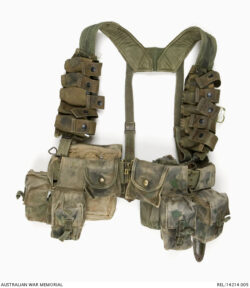Composite webbing set : Trooper D R Barnby, 2 Squadron, Special Air Service Regiment.
Description:
A composite webbing set, consisting of standard US pattern waist belt, metal buckle and 'H' harness suspender. The suspender has been modified with the addition of five nylon webbing M79 40 mm grenade pouches, cut from a US Air Force survival vest, which are attached vertically down each front suspender strap. A blackened round brass press button secures each grenade pouch cover.
Worn at the back of the belt is a large Australian 1937 Pattern basic canvas pouch and a British 1944 Pattern water bottle and carrier. In place of the standard Australian issue basic pouches at the front are twin US Special Forces M16 5.56 mm magazine pouches and two compass pouches, one containing insect repellent.
Attached to the 1937 Pattern pouch is another compass pouch, containing another insect repellent container and inside the pouch is a field dressing. The webbing set has been hand camouflaged by adding random blotches of green and black paint. A US issue plastic M6 bayonet scabbard is also attached.
AWM Accession Number: REL/14214.005 SASR Don Barnby Vietnam SAS