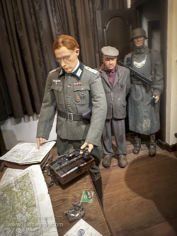 Interrogation display. The caption reads. "September 2, 1944 - At the Kommandantur of Bastogne, the Germans are nervous. The Allied forces are advancing rapidly and members of the resistance are committing more and more acts of sabotage. Close to the railroad, a person has been arrested by a German patrol. Roughly treated by the German soldiers who captured him, the alleged member of the Resistance is presented to a superior officer before being interrogated by the Gestapo. 101st Airborne Museum Bastogne